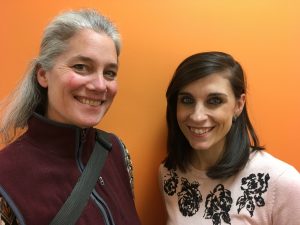 Lisa Degliantoni and Jenni Rook stand smiling in front of an orange wall