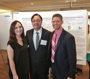 Aimee Karstens, Borna Bonakdarpour, and Jeffrey Wolfe stand smiling in front of the Musical Bridges to Memory research poster