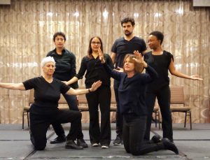 a group of six people in black creating a group tableau.