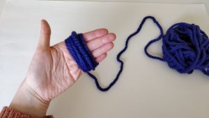 purple yarn wrapped around a person's fingers with the end string hanging off