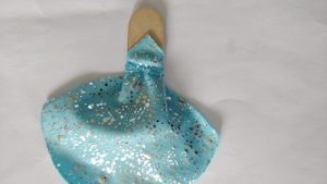 A small blue sparkly cape secured to a popsicle stick with a small elastic band.
