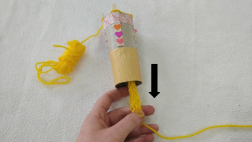 Loops of knitted yarn being pulled through a handmade french knitting doll tube.
