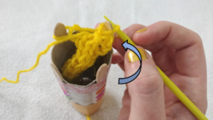 A loop of yellow thread pulled over another loop on a peg of a handmade knitting doll.