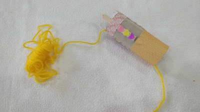 Handmade knitting doll with yellow yarn strung through the middle of the tube.