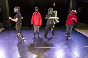4 people onstage in homemade costumes holding fake weapons and wearing masks and helmets.